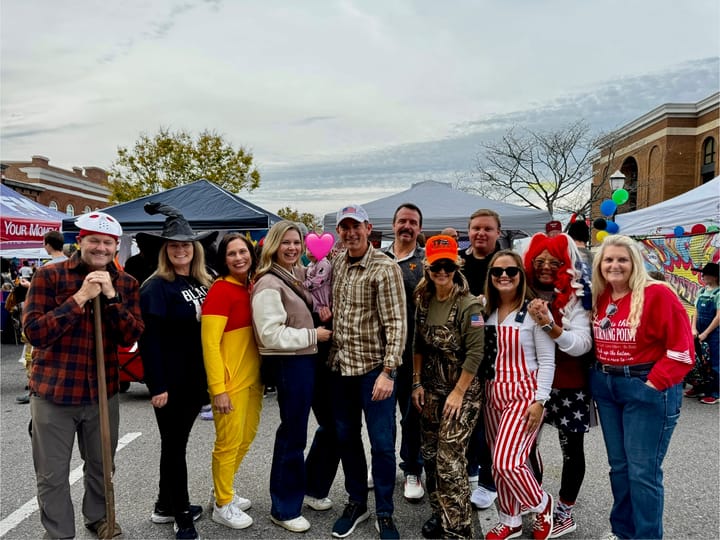 A group of attendees in Halloween costumes posing beside the event tents