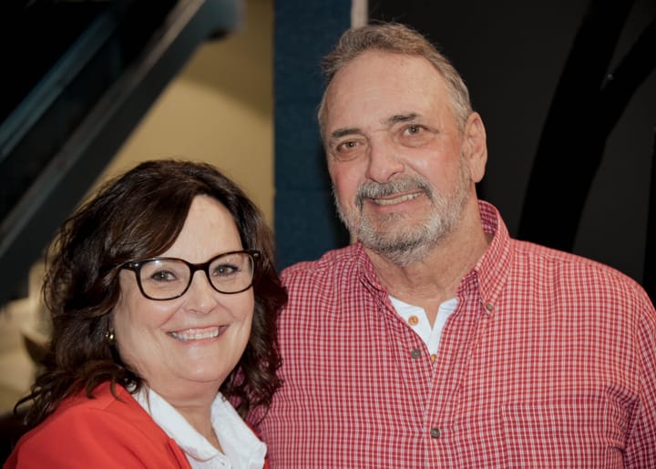 Two smiling guests in a red jacket and red checked shirt