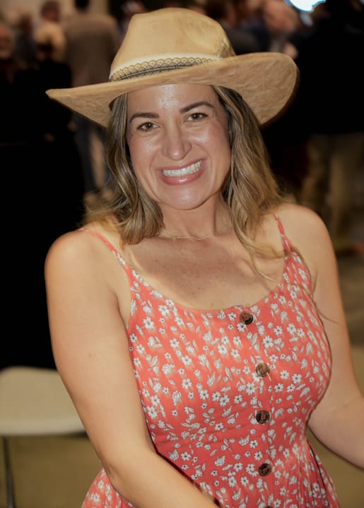 A smiling guest wearing a tan cowboy hat and floral dress