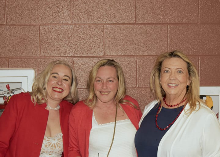 Three smiling guests standing beside a brick wall
