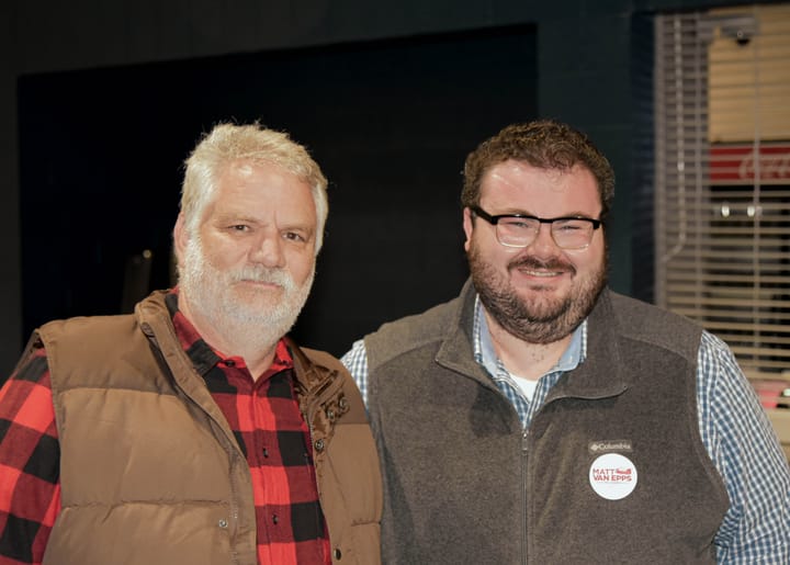 Two smiling guests wearing brown and gray vests