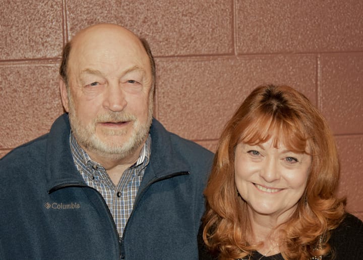 Two guests smiling together beside a brick wall