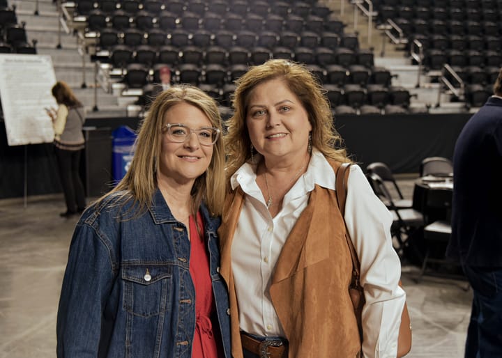 Two guests posing together in denim and a brown vest
