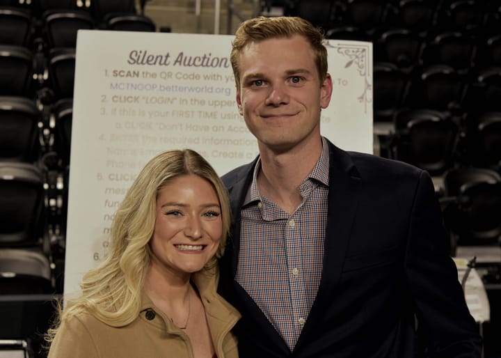 Two guests posing beside the silent auction sign