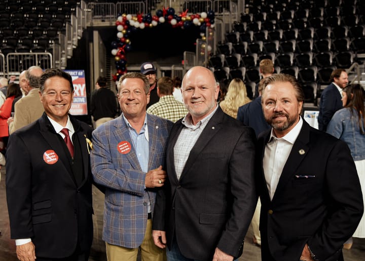 Four guests posing together in blazers on the arena floor