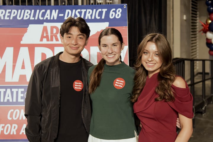 Three guests standing together in front of an event sign