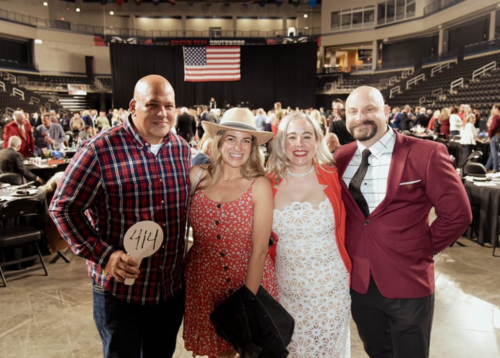 Four guests posing together, one holding a numbered auction paddle