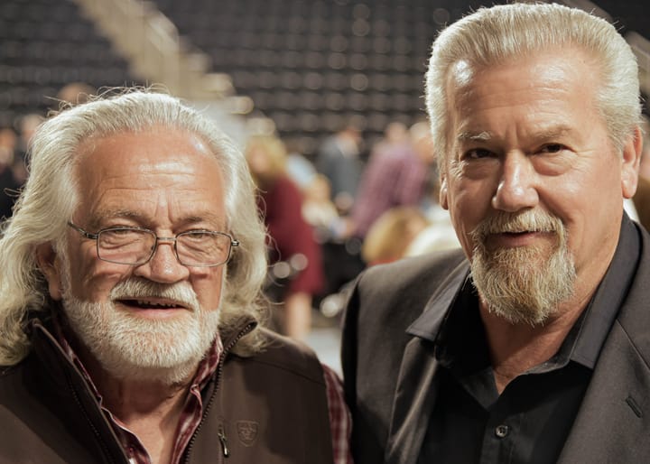 Two smiling guests posing together in front of the arena seating