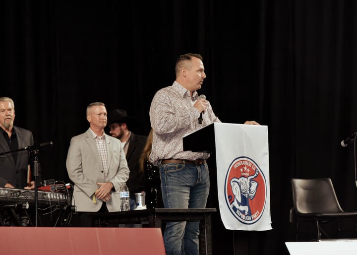 A speaker addressing the room while others stand behind the lectern