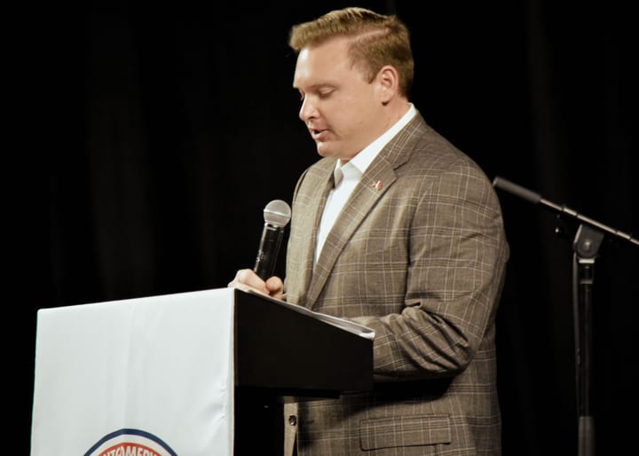 A speaker in a plaid blazer reading at the lectern