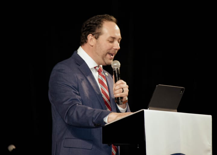 A speaker in a blue blazer reading from a tablet at the lectern