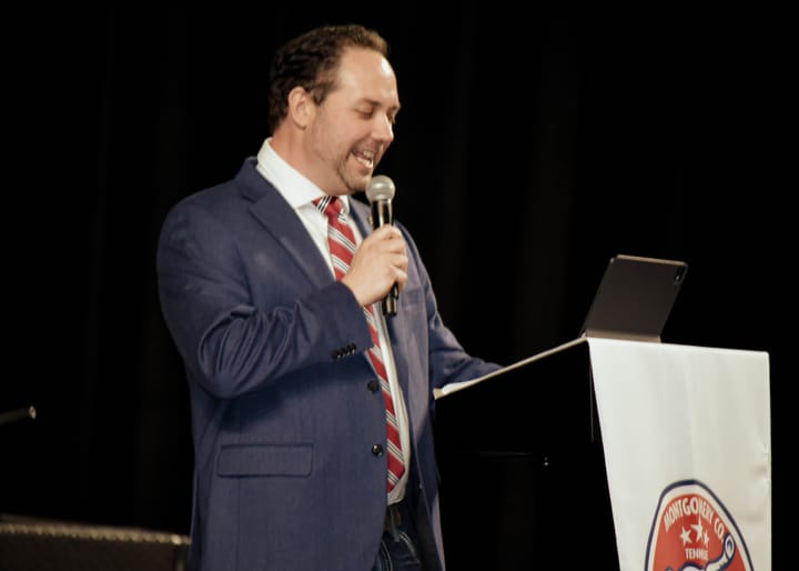A speaker in a blue blazer and striped tie holding a microphone