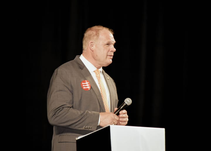 A speaker in a gray suit and orange tie holding a microphone