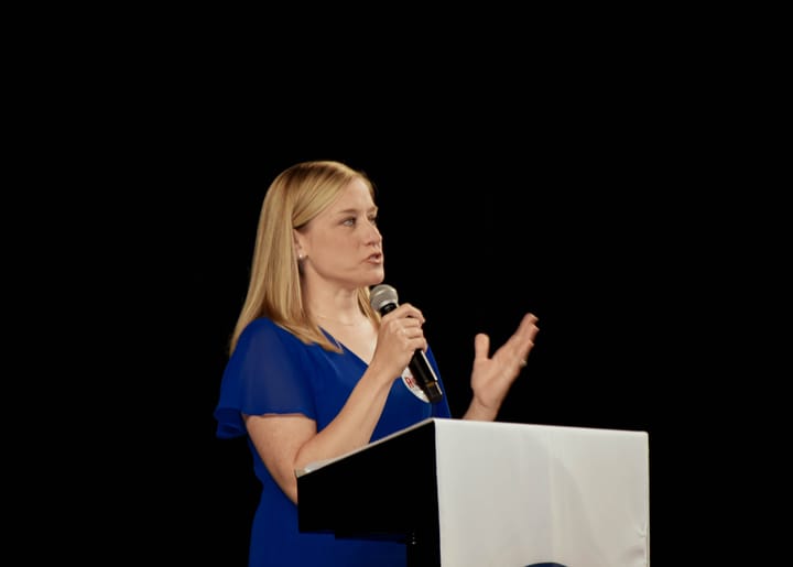A speaker in a blue dress gesturing while speaking into a microphone