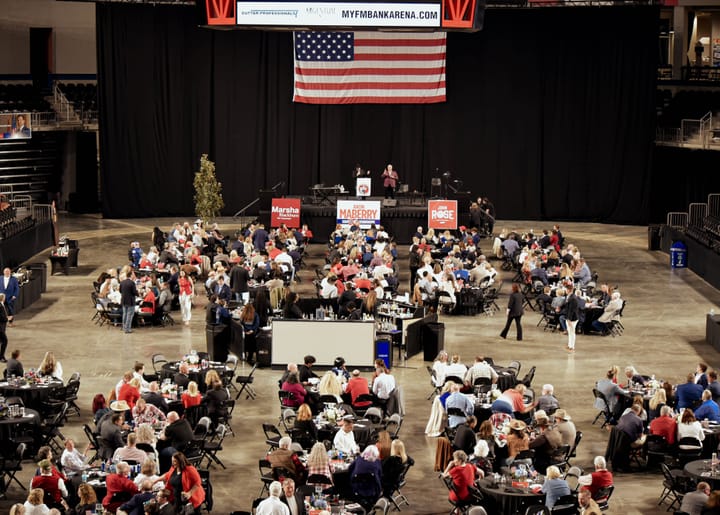 A wide arena view showing the dinner, stage, and hanging American flag