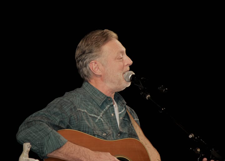 A musician singing into a microphone while playing an acoustic guitar