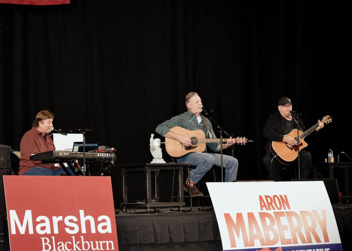 Three musicians performing on stage with a keyboard and two acoustic guitars