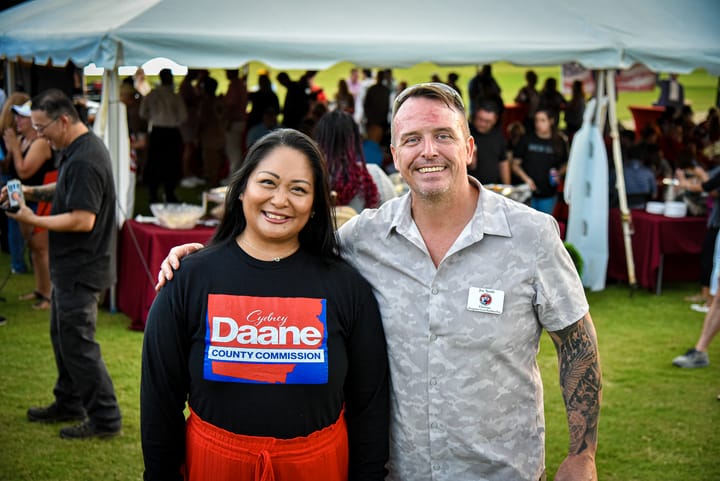 Two guests in front of the busy event tent